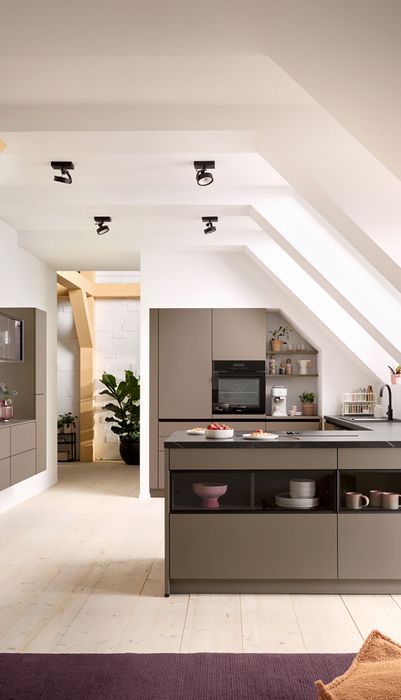 Moderne Küche mit schrägen Wänden, Holzdetails und eleganten Möbeln. Pflanzen und Dekoration sorgen für eine einladende Atmosphäre.