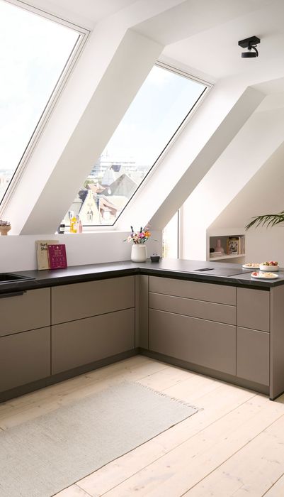 Moderne Küche mit schrägen Fenstern, grauen Schränken und einem minimalistischen Design. Pflanzen und Dekoration auf der Arbeitsfläche.