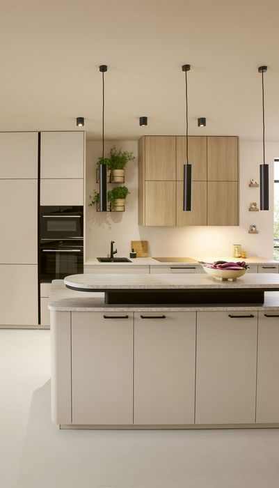 Moderne Küche mit einer zentralen Kochinsel, hellen Schränken und Holzregalen. Große Fenster sorgen für viel Tageslicht.