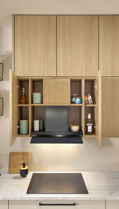 Moderne Küche mit Holzschränken, offenem Stauraum und einer Dunstabzugshaube über dem Kochfeld. Pflanzen in Töpfen sind sichtbar.