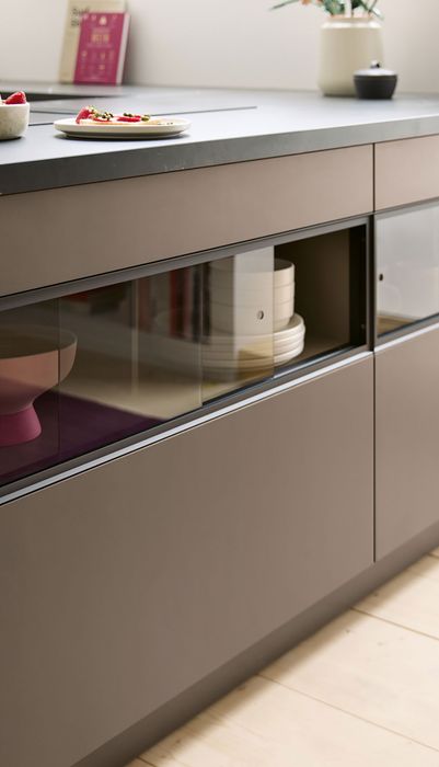 Moderne Küchenzeile mit einem dunklen, matten Finish, Glasfronten und einem Tisch mit kleinen Tellern voller Erdbeeren.