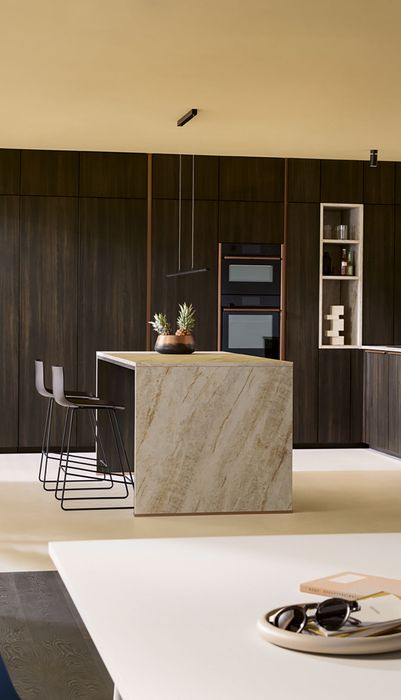 Moderne Küche mit dunklen Holzschränken, einer Kücheninsel aus Marmor und einem Essbereich mit einem Tisch und Stühlen.
