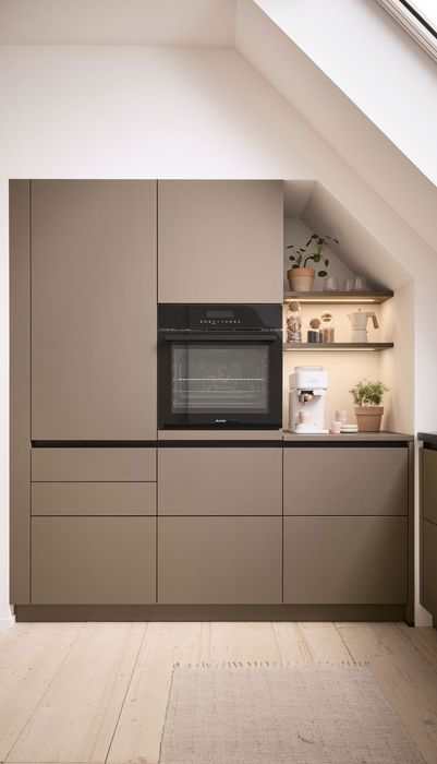Moderne Küche mit schlichten, grauen Schränken, einem eingebauten Ofen und einer kleinen Regalfläche mit Pflanzen und Dekoration.